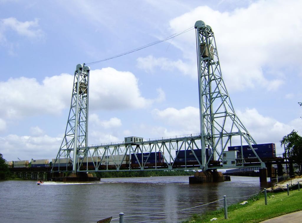 A steel vertical-lift truss railroad bridge over the Neches River at Beaumont, with a container freight train crossing between its two lift towers.